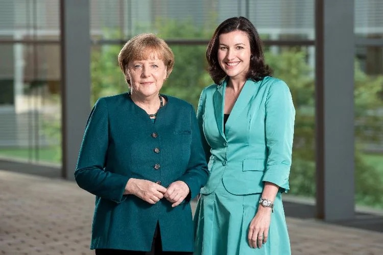 Dorothee Bär standing next to Chancellor Angela Merkel in a glass-walled building